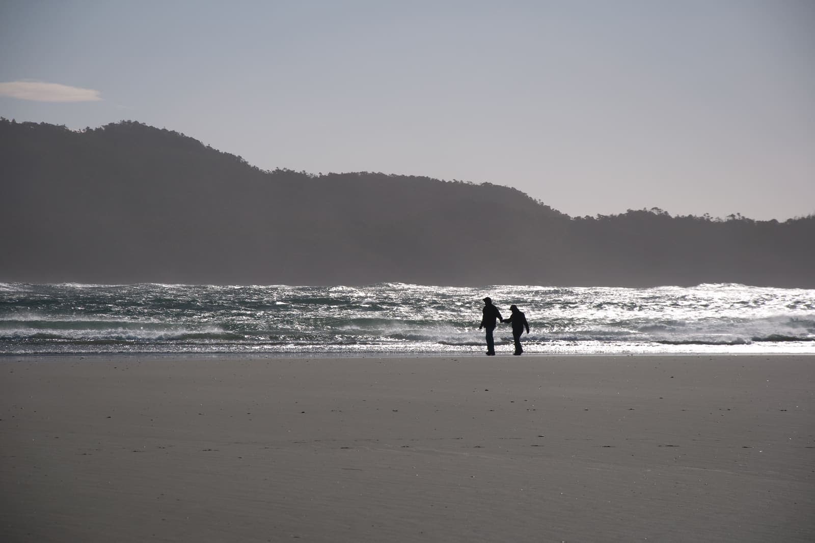 Two people walking at the water’s edge on a wide misty surf beach
